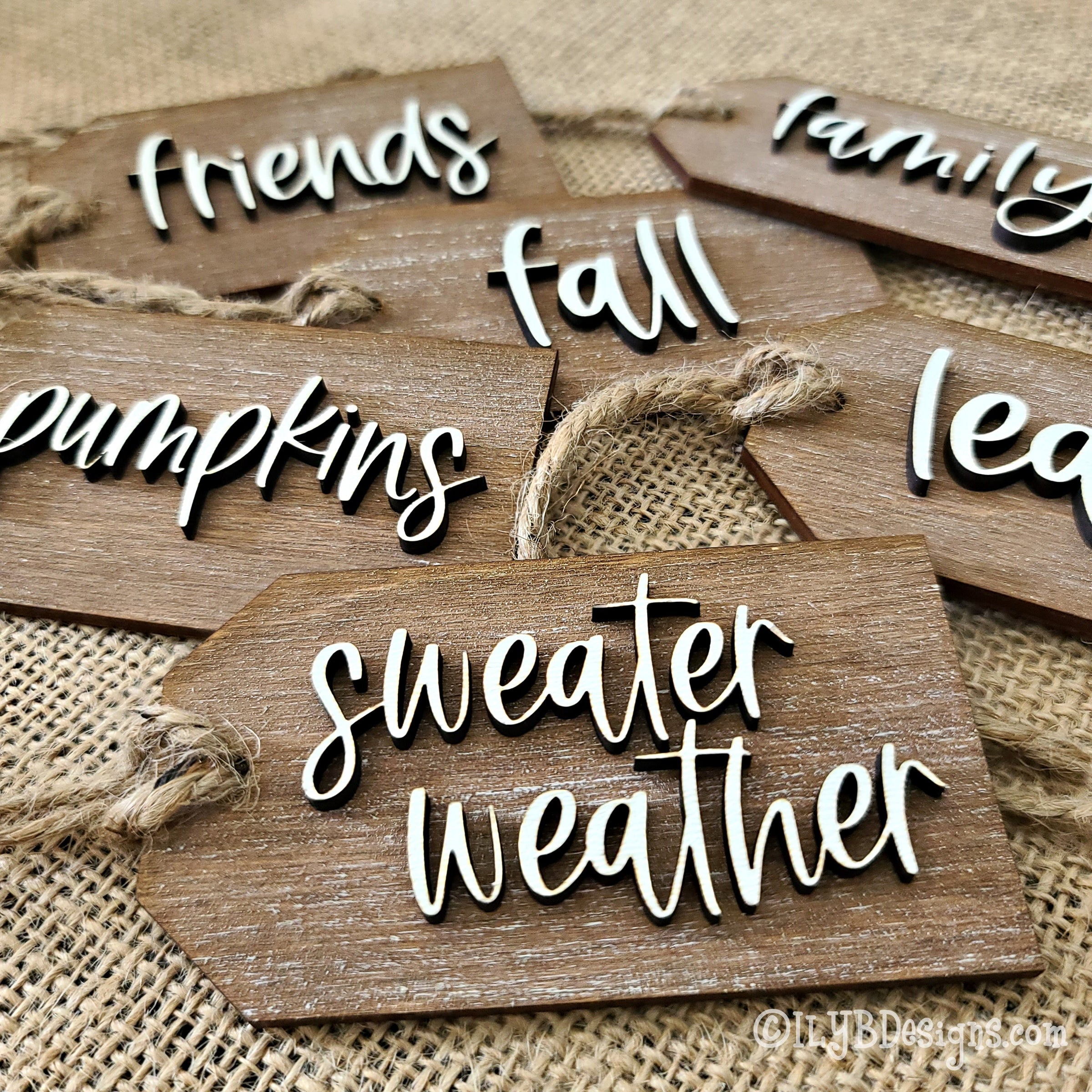 a collection of fall script words on a wood cutout tag with twine to be used as fall napkin holder