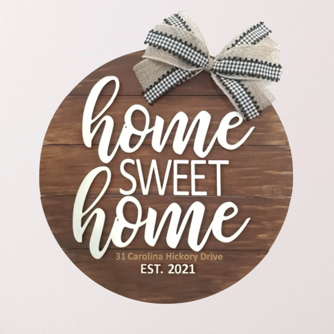 Decorative round wood sign in brown with 'home sweet home' text and a bow on top hanging on a wall above a wooden bench.