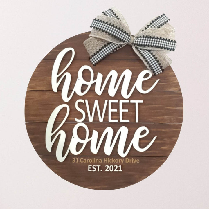 Decorative round wood sign in brown with 'home sweet home' text and a bow on top hanging on a wall above a wooden bench.