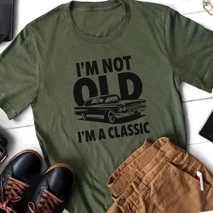 Military green t-shirt with 'I'm not old, I'm a classic' graphic and text on a white surface with shoes and pants.