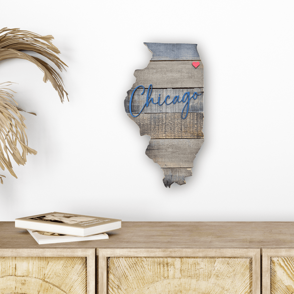 Pallet wood wall art of state of Illinois shape with blue 3D script 'Chicago' on a white wall above a wooden cabinet.