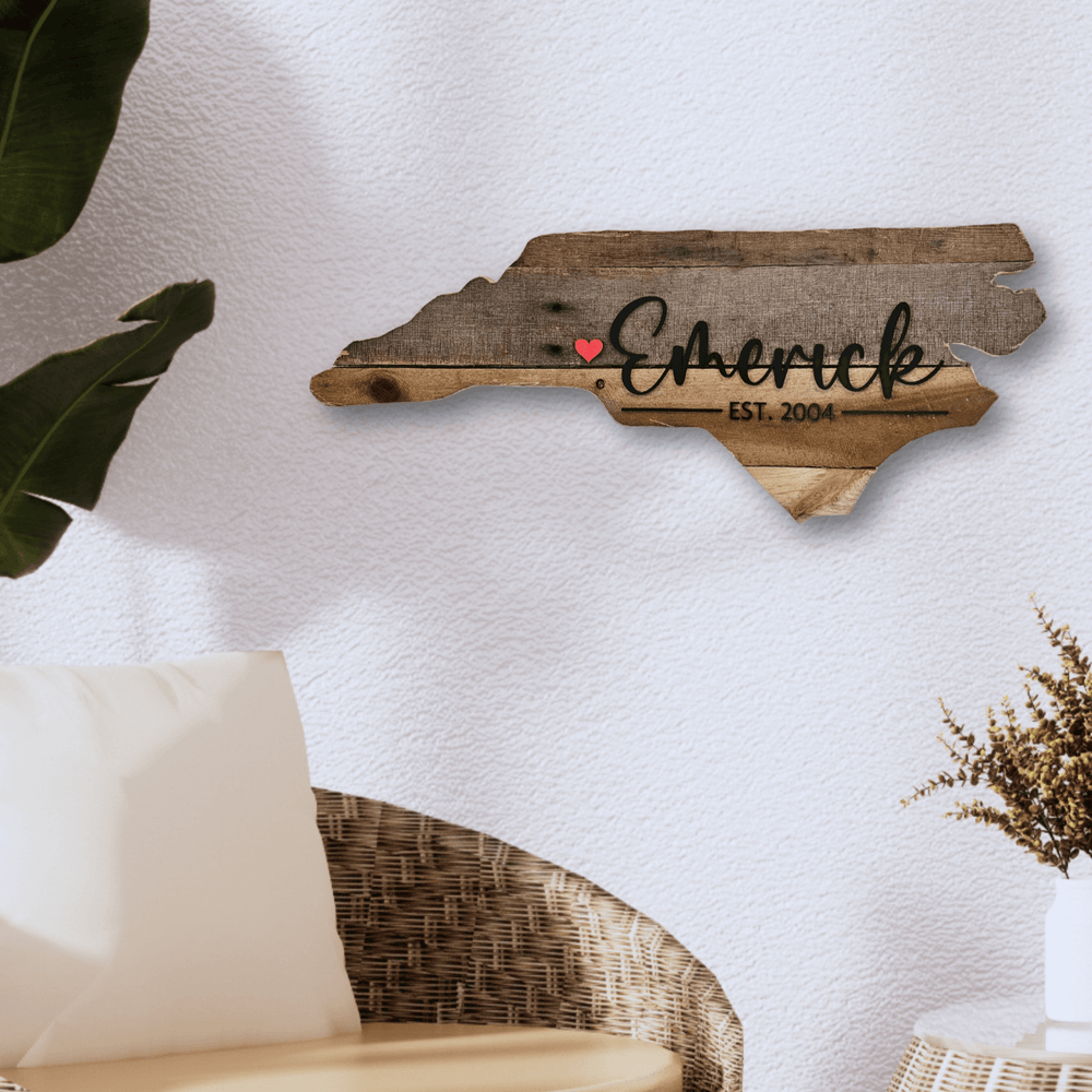 Wooden pallet wood wall decor shaped like state of North Carolina with 'Emerick' and a red heart on a white wall.