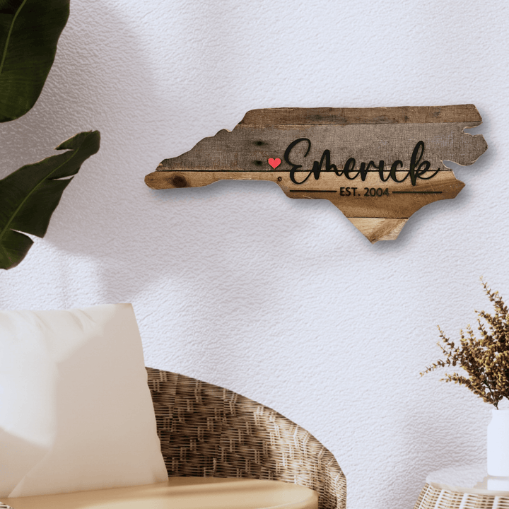 Wooden pallet wood wall decor shaped like state of North Carolina with 'Emerick' and a red heart on a white wall.