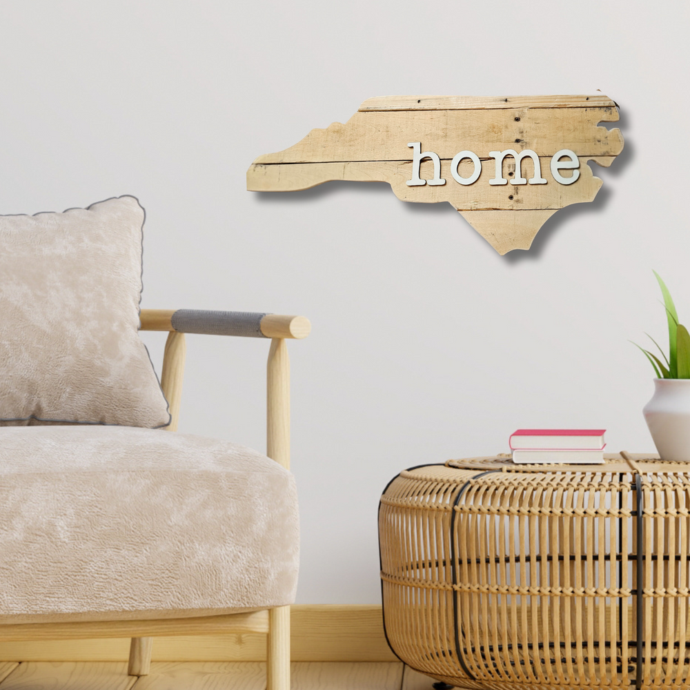 Wooden decorative sign shaped like a state with 'home' text, placed above a wicker ottoman in a living room setting.