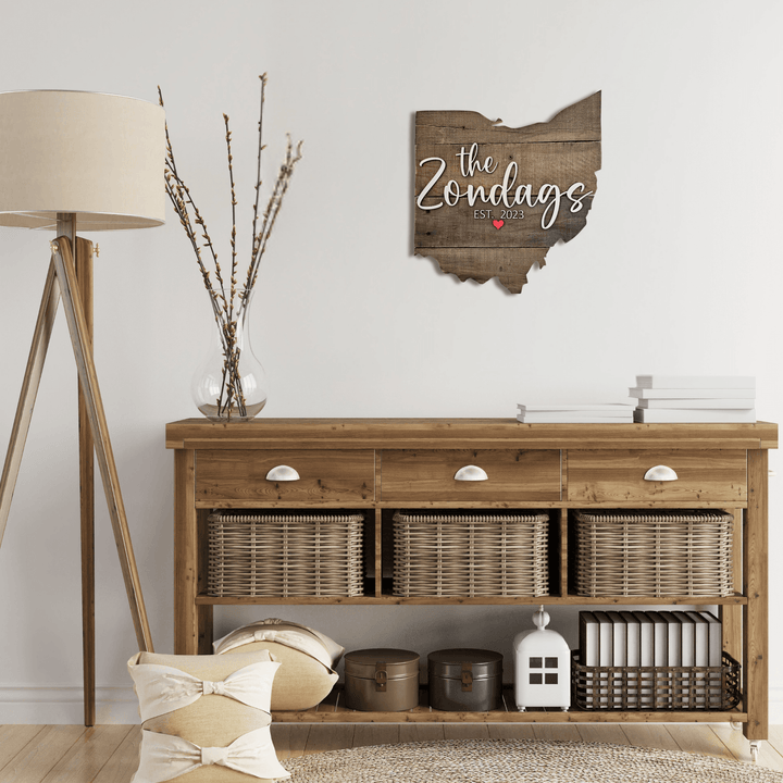 Ohio-shaped wood pallet wall decor above wooden sideboard with decorative items in a room with a wooden lamp.