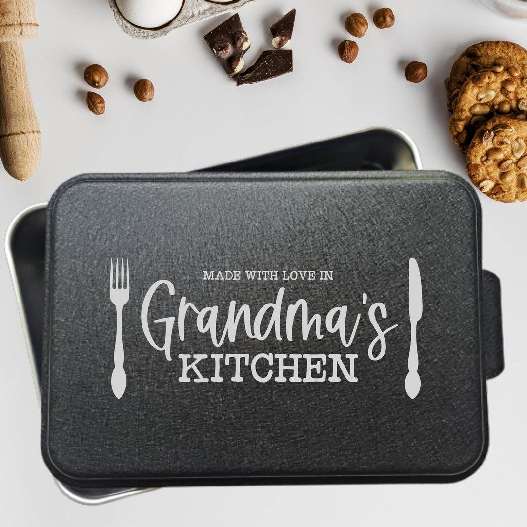 Aluminum cake pan with 'Made with love in Grandma's Kitchen' text laser engraved on a black powder coated lid on a white background with cookies and chocolate.