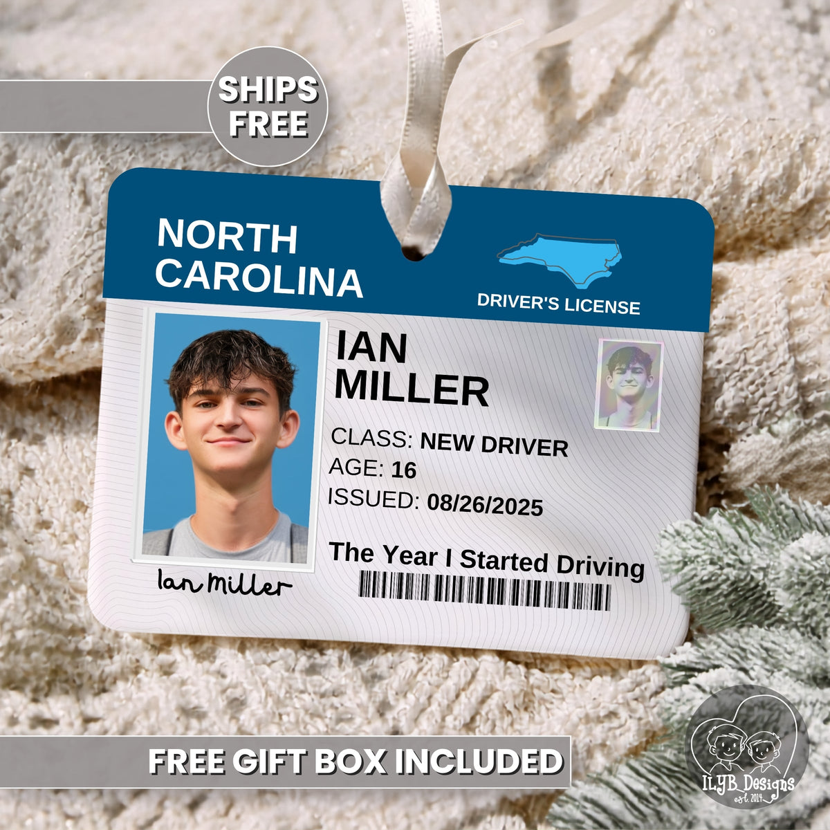 A novelty Christmas ornament shaped like a North Carolina driver's license laying on a neutral blanket with Christmas greenery in the corner. The ornament includes a sample photo, a name, and text reading 'The Year I Started Driving.'