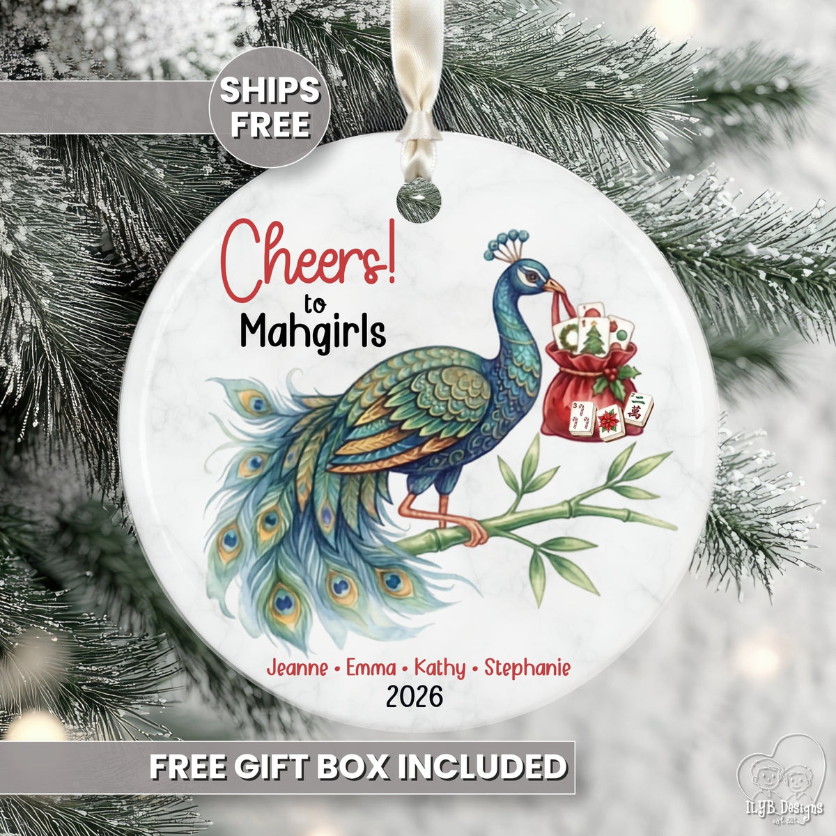 Round white Christmas ornament featuring a colorful peacock illustration and the text 'Cheers to Mahgirls' with names and the year 2026, hanging against a snowy tree background. Promotional text overlays say 'SHIPS FREE' and 'FREE GIFT BOX INCLUDED'.