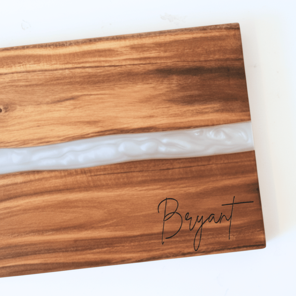 Wooden cutting board with white resin inlay and 'Bryant' engraving in the bottom right corner sitting on a white background