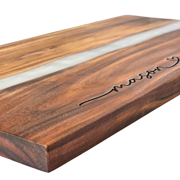 close-up wooden cutting board with a white resin inlay and engraved name on a white background