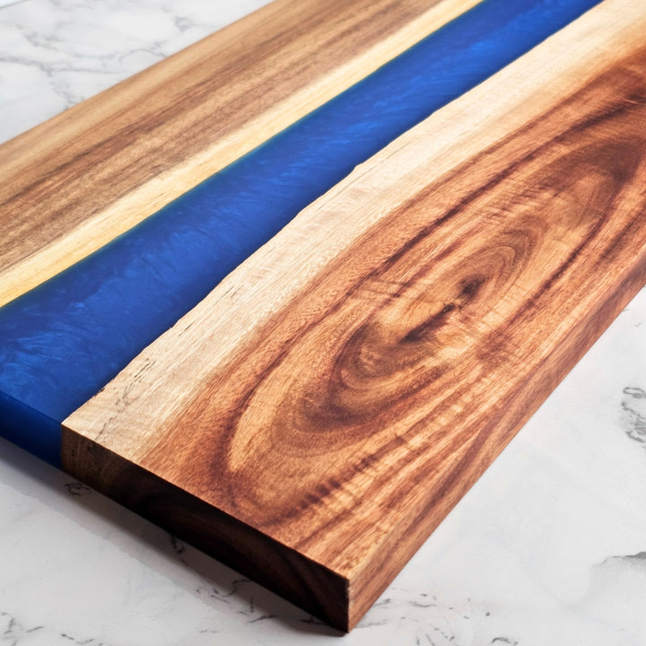 close up of wooden cutting board with blue resin inlay on a marble surface