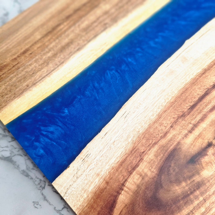 close up of wooden cutting board with blue resin inlay on a marble surface