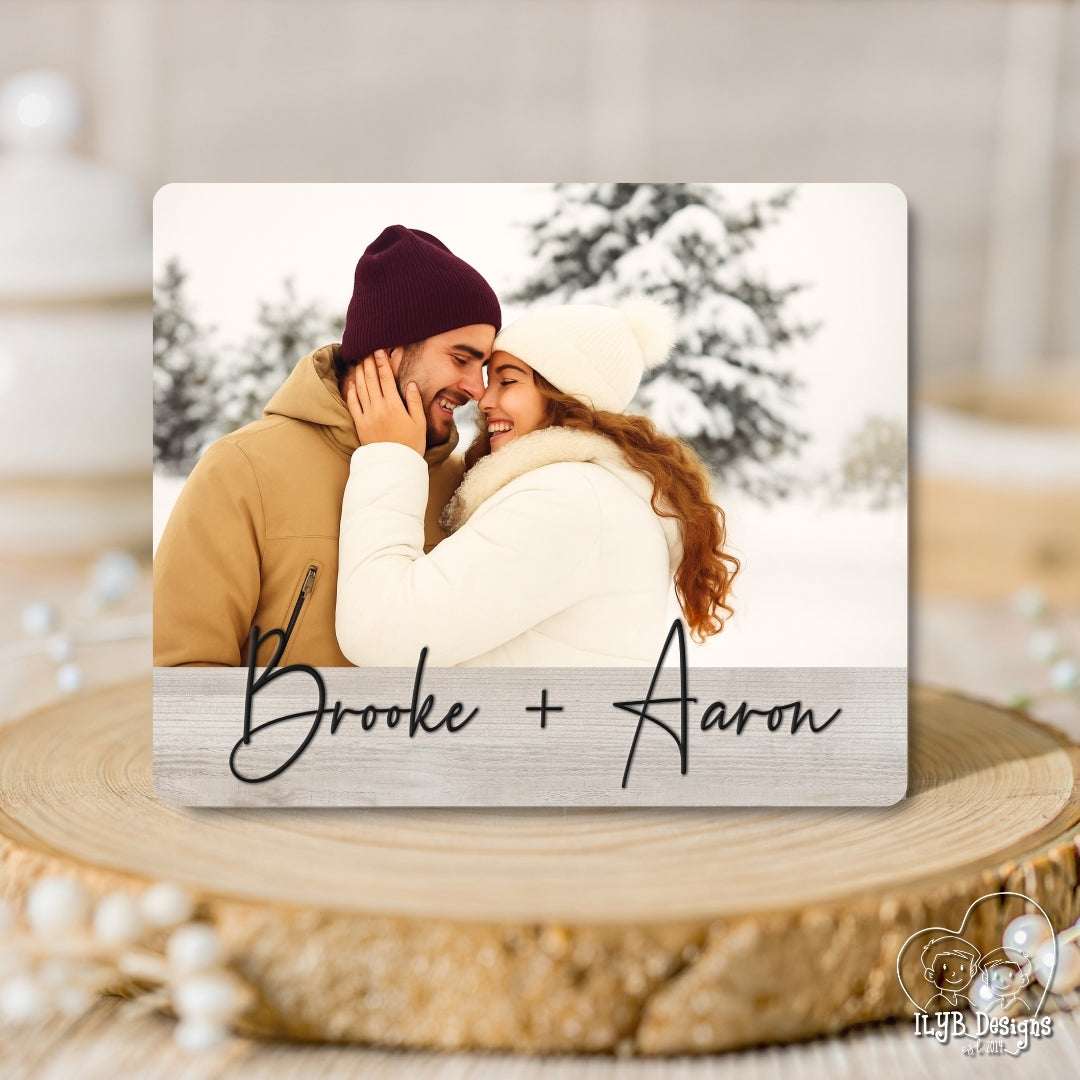 Couple in winter clothing embracing with 'Brooke + Aaron' text on a wooden surface.