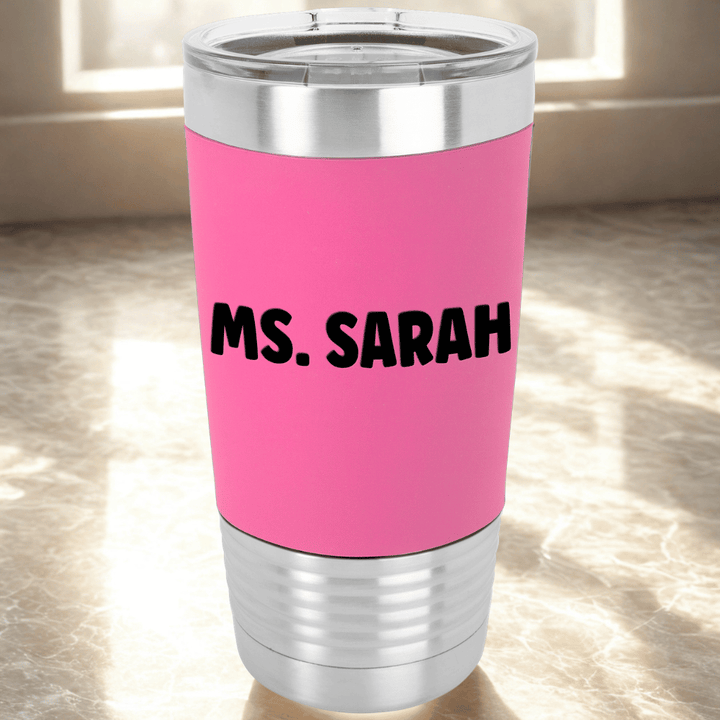 pink tumbler with 'Ms. Sarah' engraved in black sitting on a counter near a window with morning light shining through
