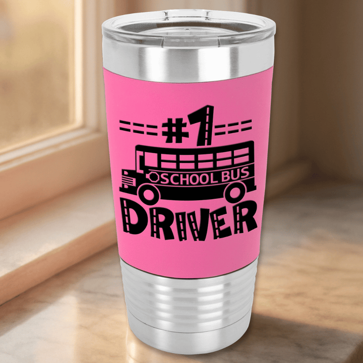 Pink tumbler with '#1 School Bus Driver' text and school bus graphic on a marble surface near a window with morning sunlight shining through
