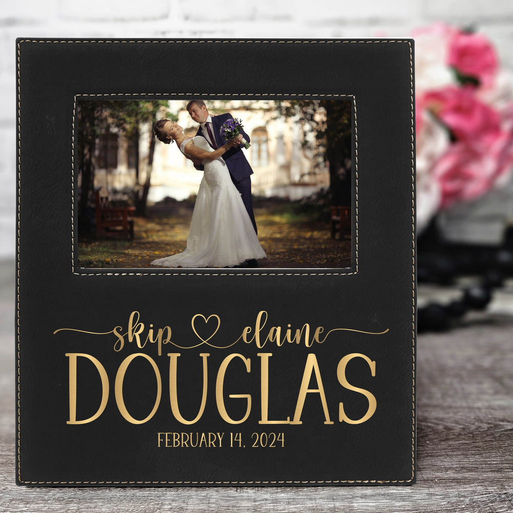 Black vegan leather wedding photo album with a couple's photo and names engraved in metallic gold on it.
