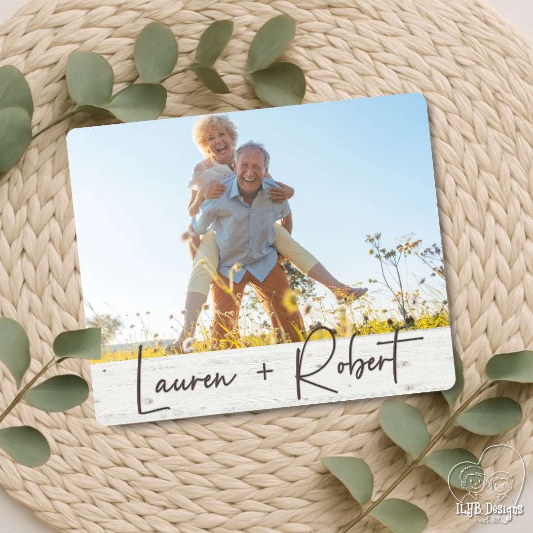 Wood photo plaque with a photo of an elderly couple and the names 'Lauren + Robert' on a woven surface with green leaves.