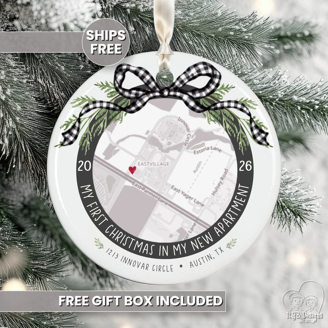 A round white Christmas ornament displayed on a snowy evergreen tree. The ornament features a black-and-white gingham bow, green pine branches, and a printed map design with the text 'MY FIRST CHRISTMAS IN MY NEW APARTMENT' and '1215 INNOVAR CIRCLE • AUSTIN, TX'.