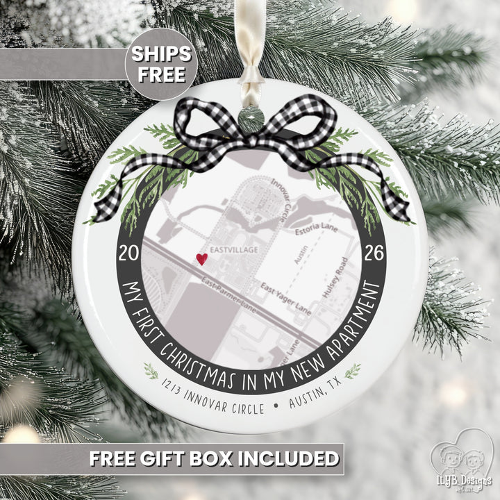 A round white Christmas ornament displayed on a snowy evergreen tree. The ornament features a black-and-white gingham bow, green pine branches, and a printed map design with the text &