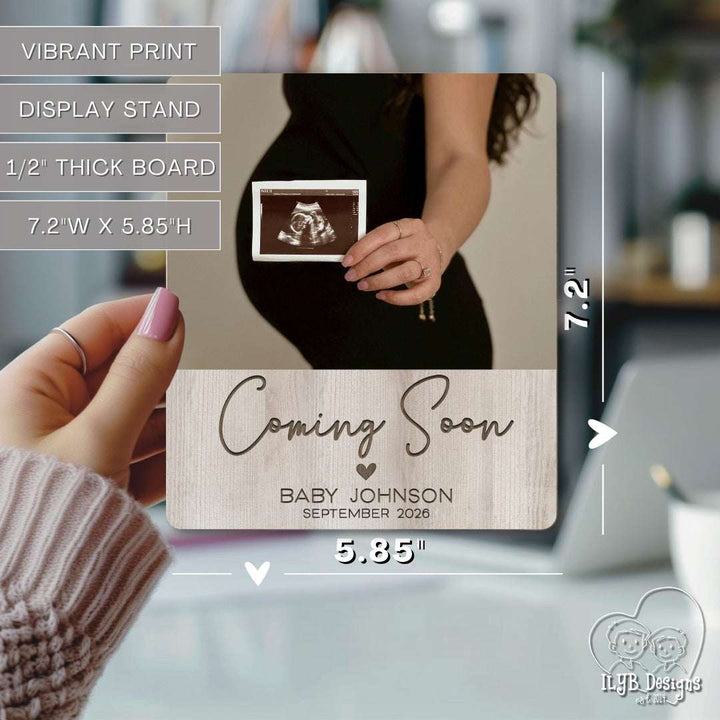 coming soon baby name announcement photo keepsake gift being held in hand to show size of 5.85 inches by 7.2 inches. Text describes photo board as having vibrant print, display stand, 1/2 inch thick board.