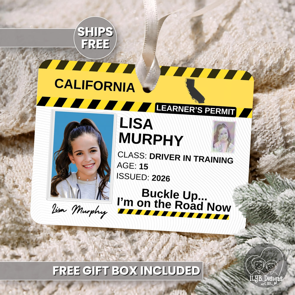 A novelty learner's permit tag styled like a California driver learner's permit, hanging against a cozy beige knit blanket background. The rectangle ornament has yellow and black hazard stripes, the text 'CALIFORNIA LEARNER'S PERMIT,' the name 'LISA MURPHY,' and phrase 'Buckle Up...I'm on the Road Now.'