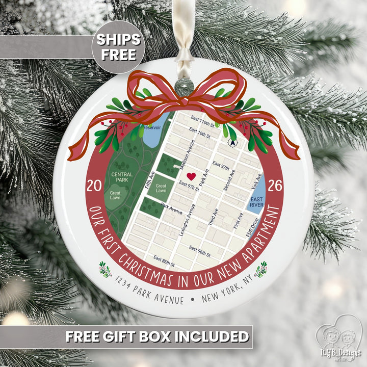 Personalized round Christmas ornament featuring a street map of a new apartment in New York City, wrapped in a red ribbon and green holly accents, hanging on a snowy Christmas tree. Text overlays read &