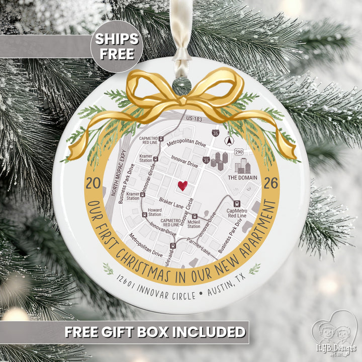 A round white Christmas ornament featuring a printed street map of a new apartment with a gold ribbon bow and green pine accents, hanging on a snowy tree. Text overlays read &