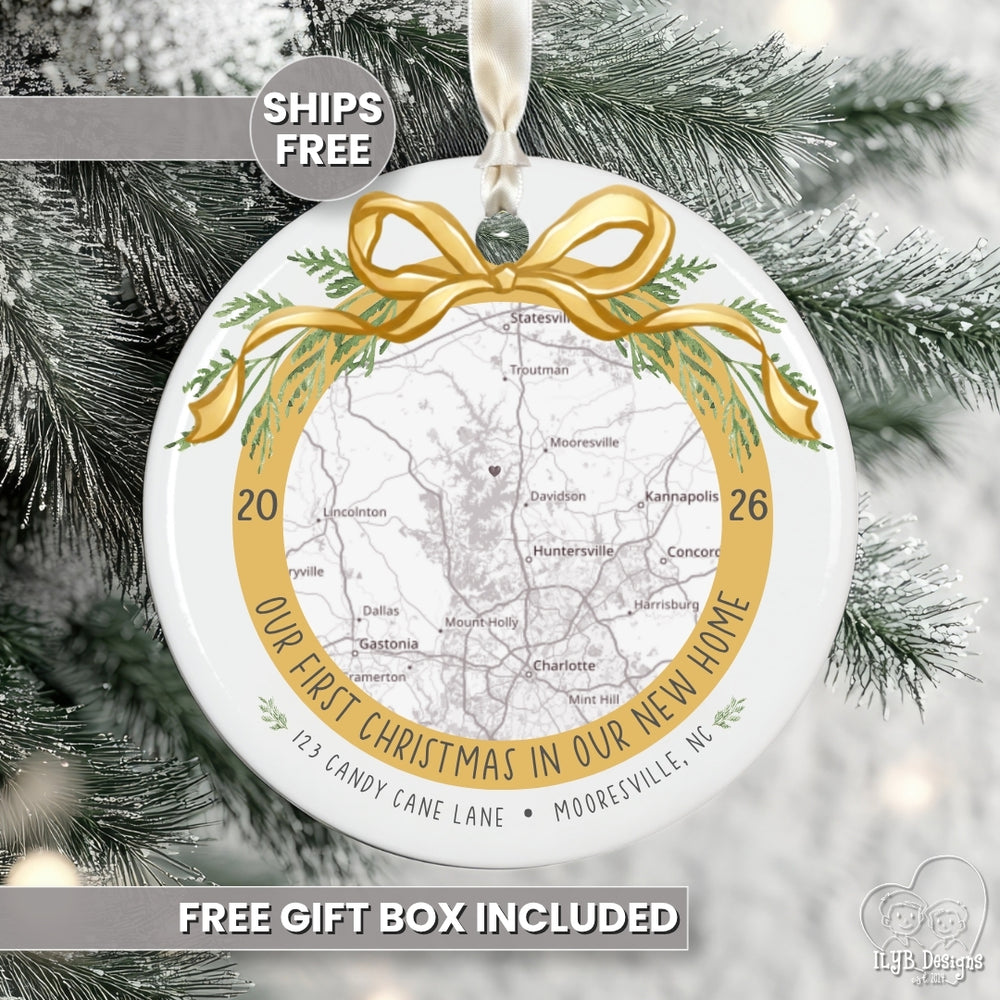 Personalized round Christmas ornament featuring a map of a home with a gold ribbon and green pine accents and the phrase 'Our First Christmas in Our New Home', hanging on a snowy Christmas tree. Text overlays read 'SHIPS FREE' and 'FREE GIFT BOX INCLUDED'.