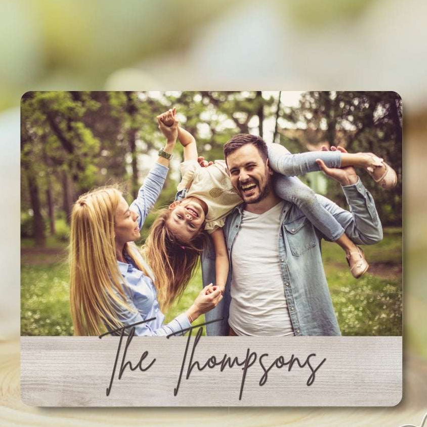Family photo on a wooden plaque with 'The Thompsons' text, set against a blurred natural background.