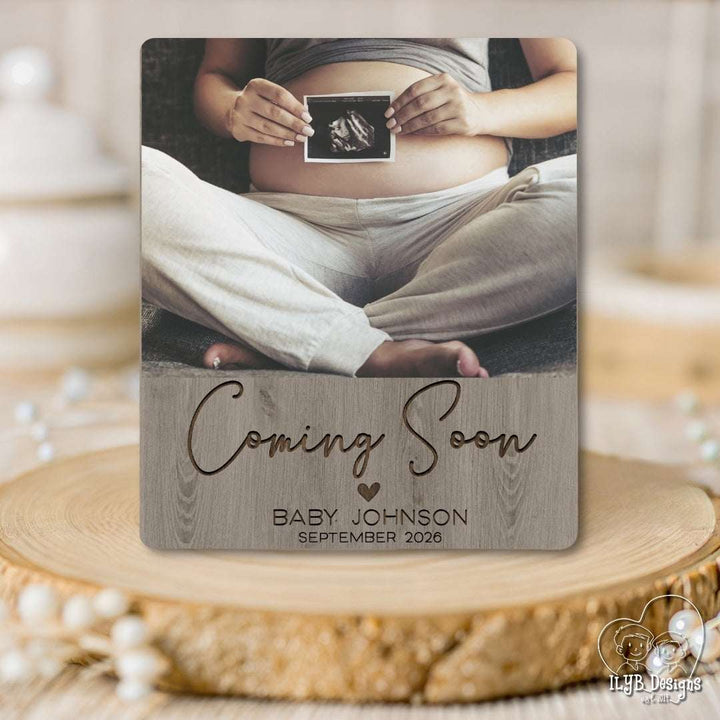 Coming soon baby name announcement photo keepsake gift with photo of pregnant woman holding sonogram picture and text 'coming soon baby johnson' with month and date in text below photo that looks engraved on a grayish wood background