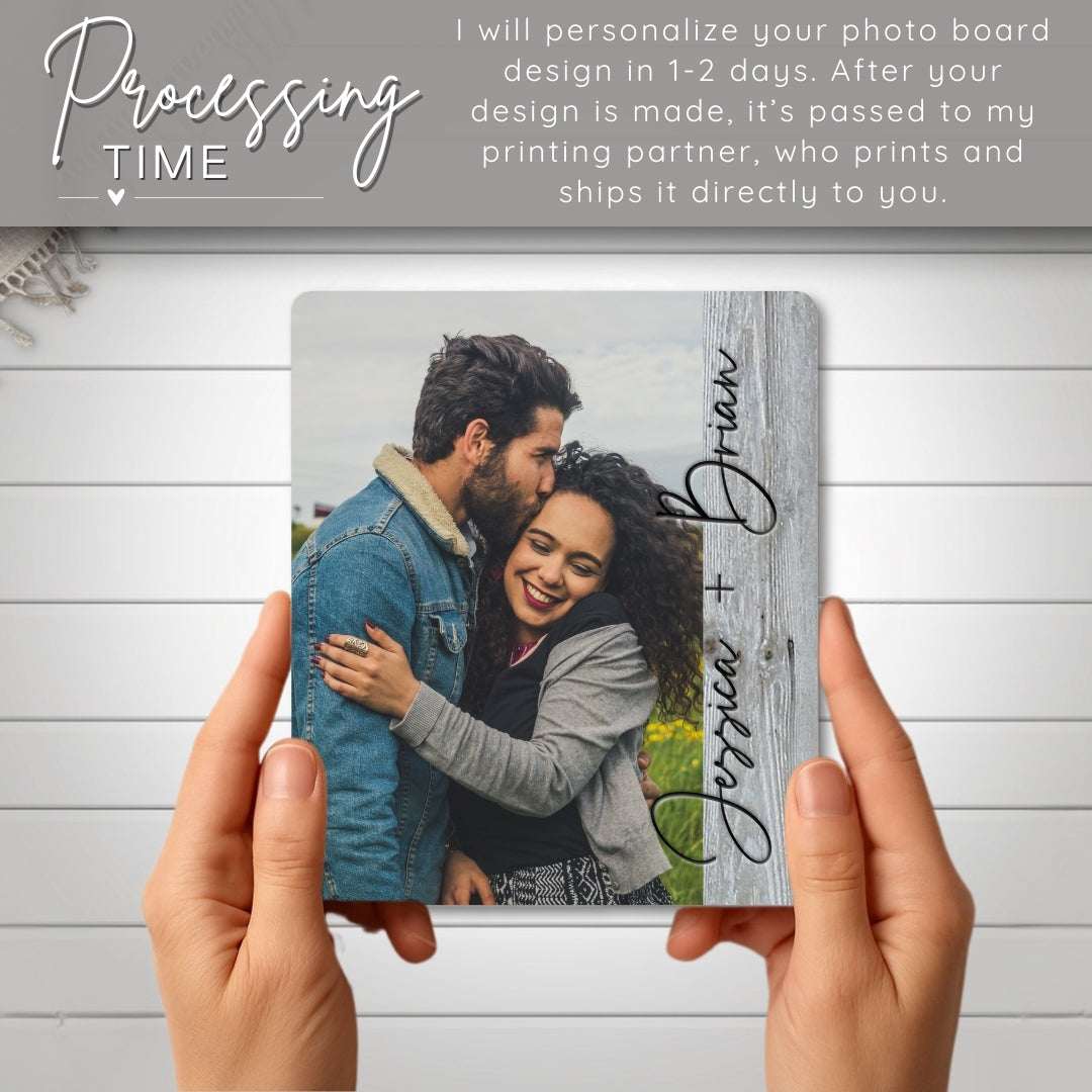 Person holding a photo board with a couple's picture and names on a wooden surface.