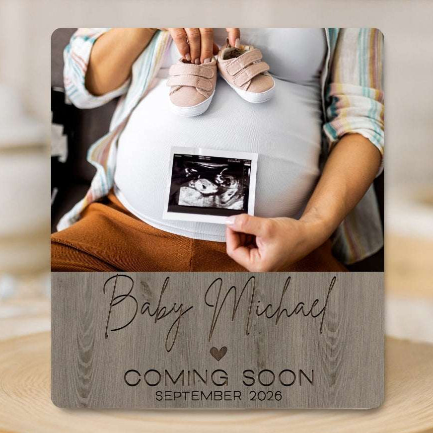 Pregnant belly with baby shoes and ultrasound photo, 'Baby Michael Coming Soon September 2023' text on a wooden surface.