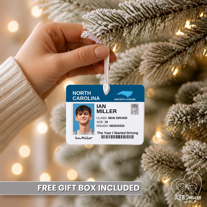 A hand holds a frosted Christmas tree branch while wearing a white knit sweater. The branch is decorated with a white ornament shaped like a North Carolina driver&
