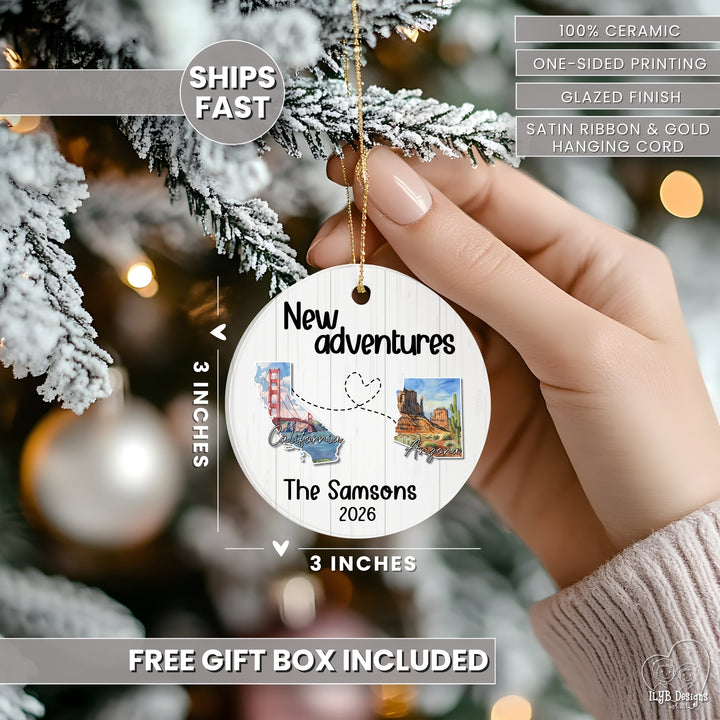 A hand holds a round white ceramic Christmas ornament against a blurred Christmas tree background. The ornament is personalized with the text &