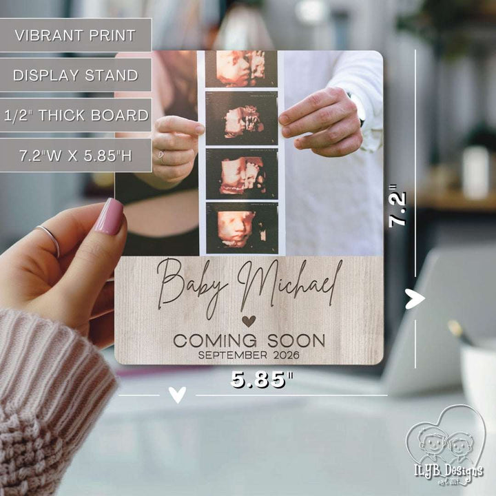 Baby announcement photo board held by a hand with dimensions displayed