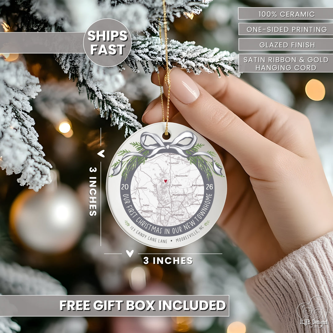 A hand holds a round ceramic Christmas ornament against a blurred Christmas tree background. The ornament features a vintage-style map design with green holly leaves, a bow illustration, and text reading &