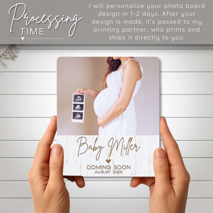 Person holding a personalized photo board with text 'Baby Miller Coming Soon August 2023' on a wooden surface.