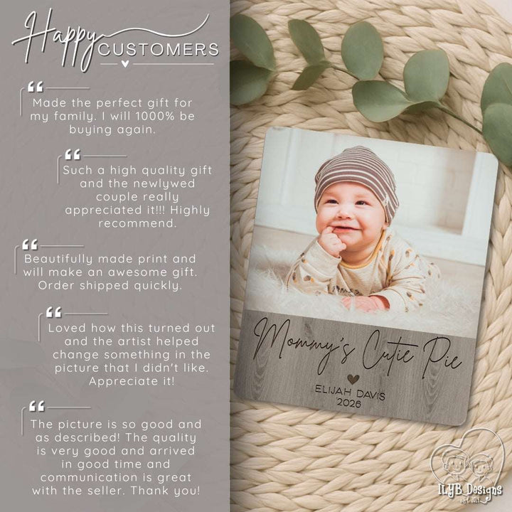 Wooden photo plaque with a baby photo and engraving, surrounded by eucalyptus leaves on a textured surface.