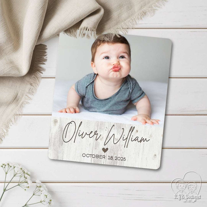 Baby photo on a wooden plaque with 'Oliver William' and date, on a wooden surface with a blanket.
