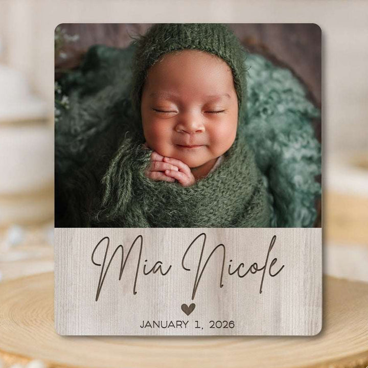 Newborn baby in green wrap with 'Mia Nicole' and birth date on a wooden block