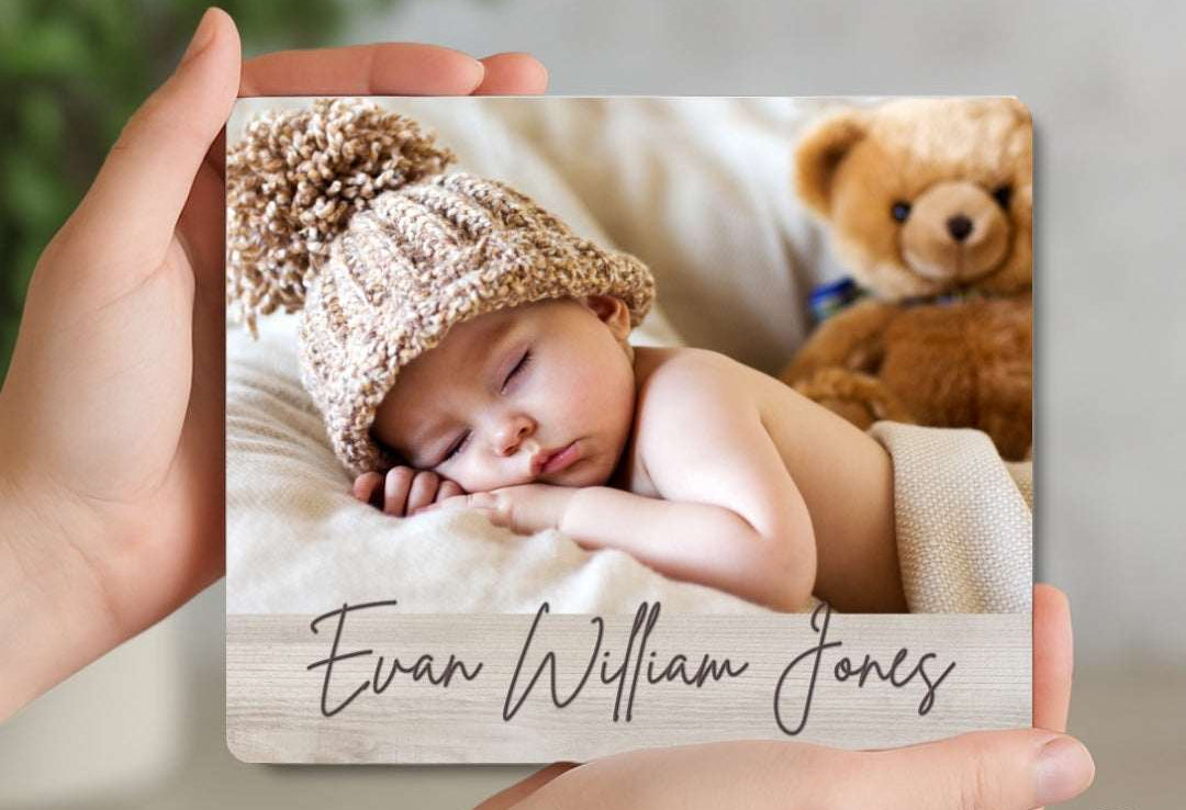 Person holding a photo of a baby with a name engraved, surrounded by a teddy bear.