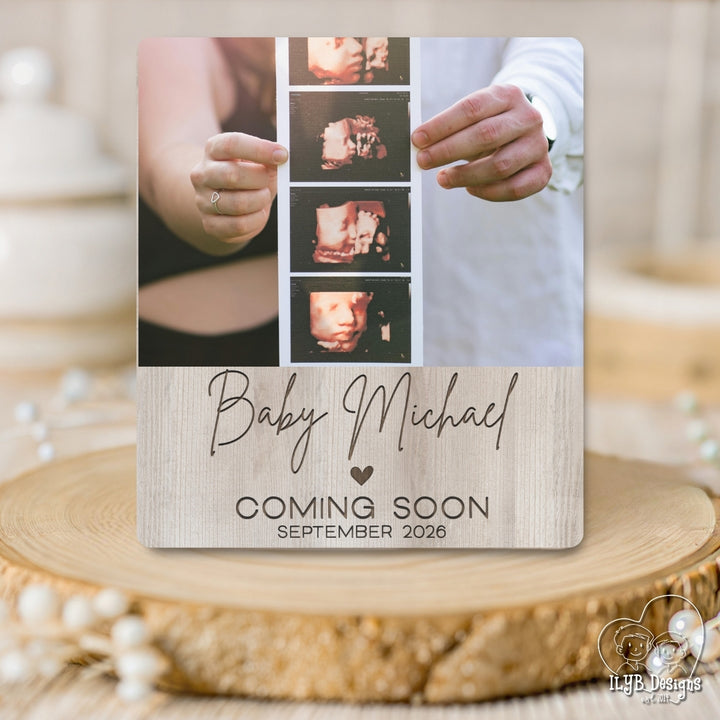 Baby announcement photo board with ultrasound images and 'Baby Michael' text on a wooden surface.