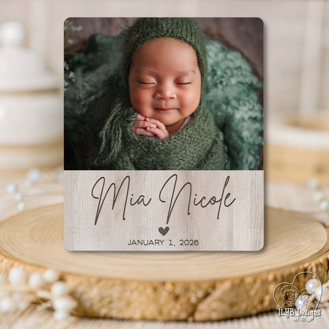 Newborn baby in green wrap with 'Mia Nicole' and birth date on a wooden block
