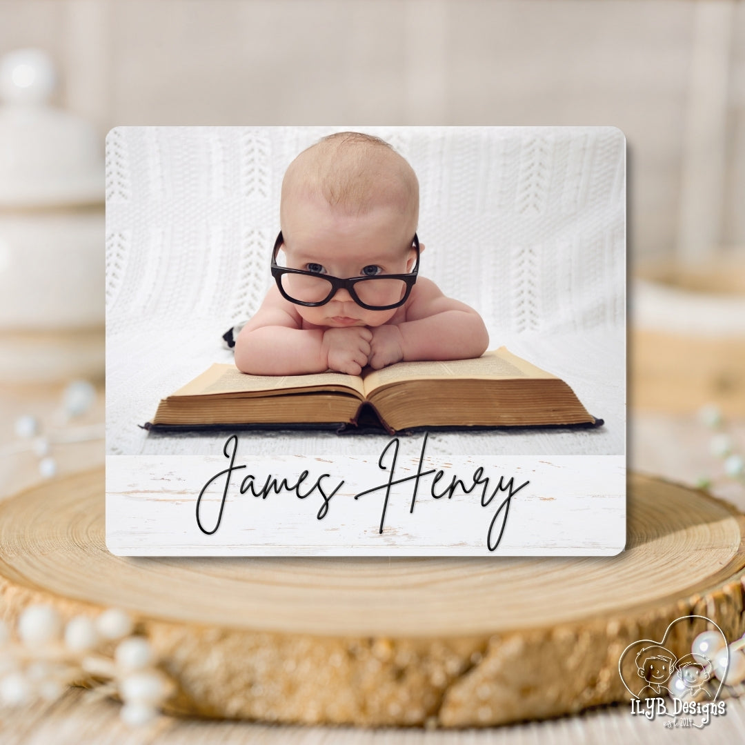Baby wearing glasses on an open book with 'James Henry' text, placed on a wooden surface.