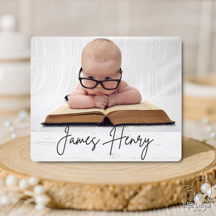 Baby wearing glasses on an open book with 'James Henry' text, placed on a wooden surface.