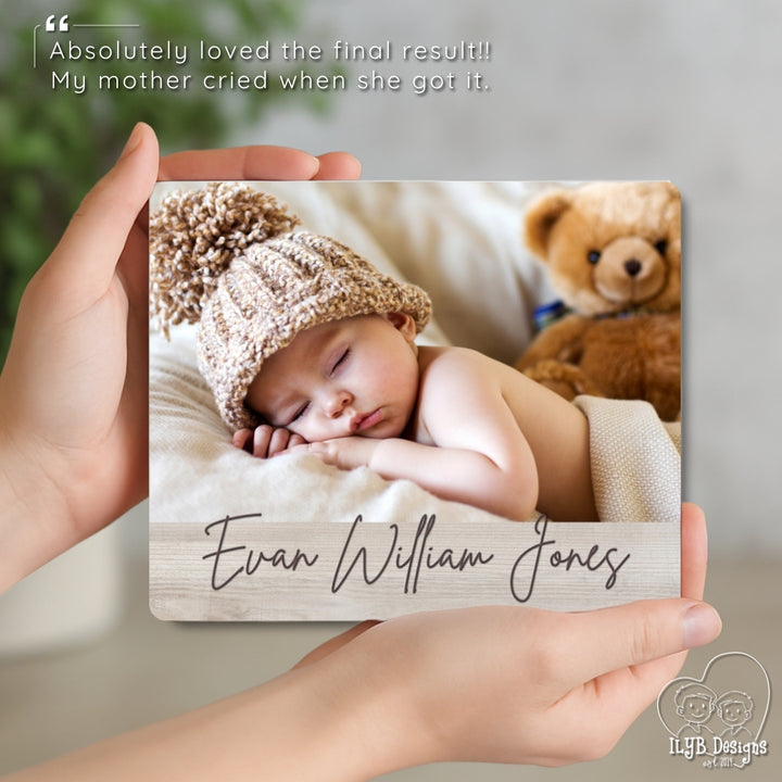 Person holding a photo of a baby with a name engraved, surrounded by a teddy bear.