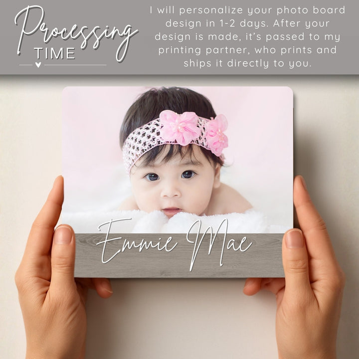 Person holding a photo board with a baby's face and name 'Emmie Mae' on a light background.