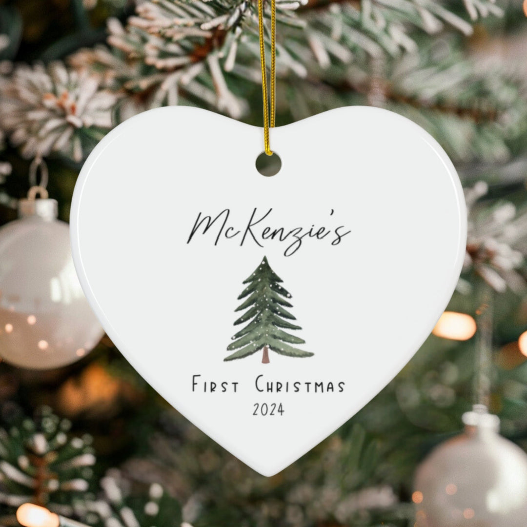 Heart-shaped ornament with 'McKenzie's First Christmas 2024' text and tree design, hanging on a decorated Christmas tree.