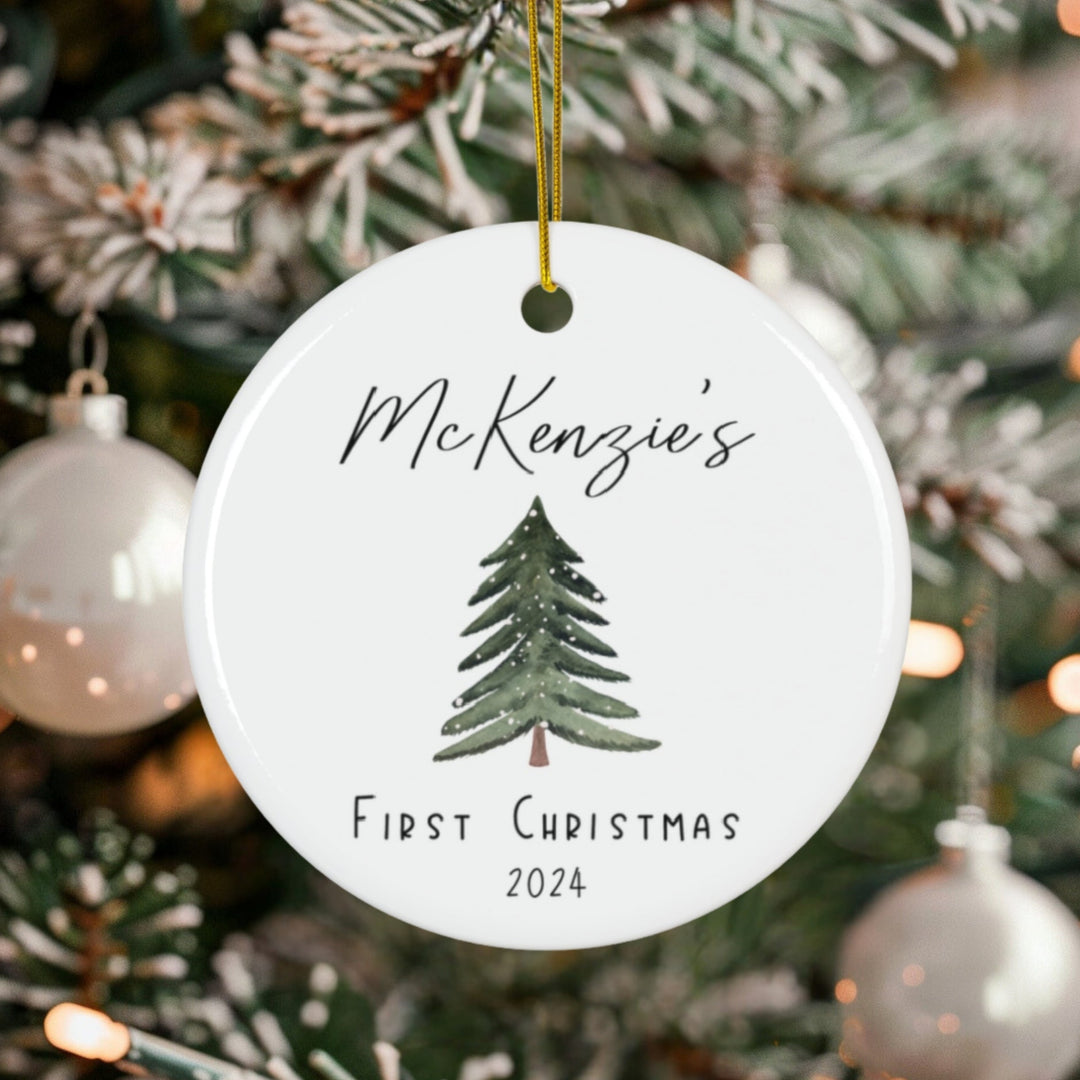 Personalized Christmas ornament with a tree design and a baby's name along with the words First Christmas and the year, hanging on a decorated tree.