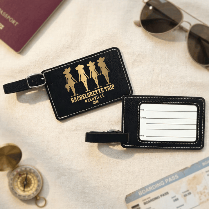 Front and back of black luggage tags with gold text on a textured surface with travel items.